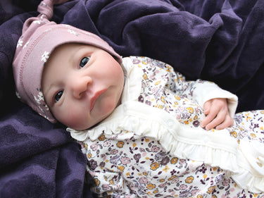 A baby dressed in floral rests on a cozy blanket, with a peaceful expression